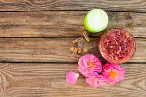 marmellata barattolo, viso crema, bottiglia di essenziale olio di rosa petali su di legno sfondo. foto