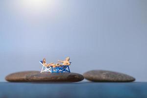 persone in miniatura che prendono il sole su una spiaggia, concetto di estate foto