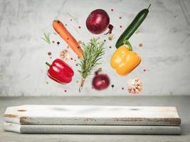 fresco verdure cipolle, carote, giallo e rosso peperoni, un' mazzo di rosmarino levitare su un' grigio sfondo al di sopra di un' di legno taglio tavola foto