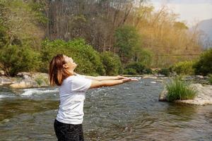 asiatico donna a piedi nel il flusso, spruzzi acqua. lei è felice, fresco e rilassato per Esperienza natura, flussi, montagne e fresco aria a il nazionale parco. foto