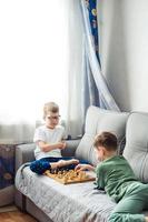 ragazzi giocando di legno scacchi dire bugie su un' grigio divano nel davanti di il finestra foto