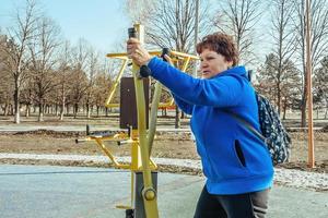 un' pensionato donna con un' zaino su sua le spalle su un attivo camminare all'aperto è impegnato nel esercizio attrezzatura nel il parco. anziano donna assunzione cura di sua Salute foto