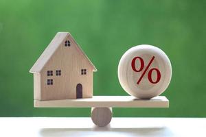 modello di casa con un'icona del simbolo di percentuale su una scala di legno su uno sfondo verde naturale, tasso di interesse in aumento e concetto bancario