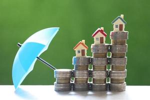 case modello su pile di monete con un ombrello su uno sfondo verde natura, assicurazione finanziaria e concetto di investimento sicuro foto