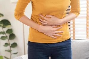 flatulenza asiatico giovane donna, ragazza mano nel stomaco dolore, soffrire a partire dal cibo avvelenamento, addominale dolore e colon problema, gastrite o diarrea. paziente gonfiarsi, addome o infiammazione, concetto. foto