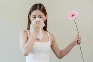 allergico rinite sintomo di odore polline fioritura, ritratto asiatico giovane donna mano nel starnuto, soffiaggio che cola naso dopo odore, puzzolente a partire dal fioritura fiore, Tenere lontano rosa flora su bianca sfondo. foto