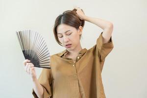 sofferenza estate calore ictus, caldo tempo atmosferico, stanco asiatico giovane donna, ragazza sudato e assetato, rinfrescante con mano nel soffiando, onda fan per ventilazione quando temperatura alto a casa, casa.su sfondo foto