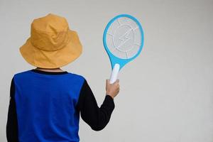 indietro Visualizza di ragazzo indossa cappello, blu camicia, detiene zanzara elettrico scacciamosche racchetta. concetto, elettrico dispositivo per uccidere zanzare, insetti, bug di schiacciando per volante insetti foto