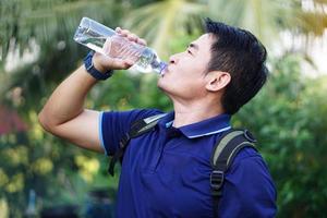 bello asiatico uomo viaggiatore detiene bottiglia di potabile acqua per bevanda all'aperto. concetto ,potabile acqua per Salute, salutare stile di vita.spegnere sete, ridurre fatica, rinfresca corpo. foto