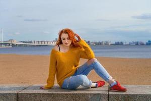 giovane dai capelli rossi ragazza nel giallo maglione e jeans. bella donna si siede foto