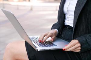 giovane grave attività commerciale donna con il computer portatile studiando in linea mentre seduta su panchina foto