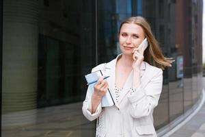 un' bellissimo bionda ragazza detiene un' smartphone e un' taccuino nel sua mani. foto