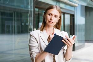 attività commerciale donna nel leggero giacca sta e scrive qualcosa vicino attività commerciale foto