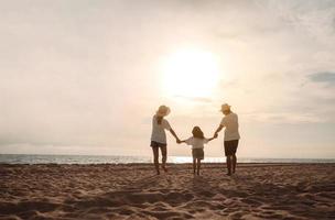 contento asiatico famiglia godere il mare spiaggia a consistente padre, madre e figlia avendo divertimento giocando spiaggia nel estate vacanza su il oceano spiaggia. contento famiglia con vacanze tempo stile di vita concetto. foto