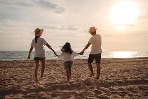 contento asiatico famiglia godere il mare spiaggia a consistente padre, madre e figlia avendo divertimento giocando spiaggia nel estate vacanza su il oceano spiaggia. contento famiglia con vacanze tempo stile di vita concetto. foto