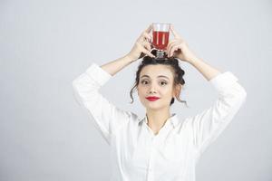 bella donna in un vestito bianco che tiene un bicchiere di succo rosso in cima alla sua testa foto