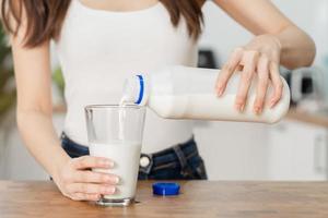 asiatico sottile giovane donna, ragazza scrosciante di fresco, latteria latte a partire dal bottiglia in bicchiere o tazza, potabile e mangiare prima colazione nel mattina a cucina casa. calcio, proteina per salutare stile di vita le persone. foto