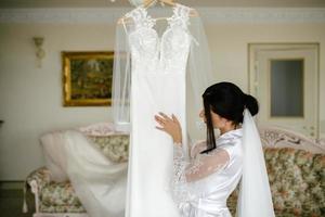 mattina di il sposa. della sposa commissioni. il sposa ammira e tocchi sua vestito foto