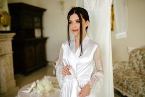 romantico atmosfera di il della sposa mattina. sposa nel un' casa. sposa mattina preparazione. sposa nel bellissimo vestito vicino il indossatrice con vestito in casa a casa. godere ogni momento. foto