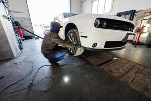 meccanico nel servizio riparazione stazione Lavorando con muscolo macchina. uomo lavoratore jack su il auto per diagnosticare il telaio. foto