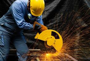 lavoratore tagli metallo di elettrico circolare sega. Fontana di macinazione metallo scintille. metallo Lavorando con personale protettivo attrezzatura. foto