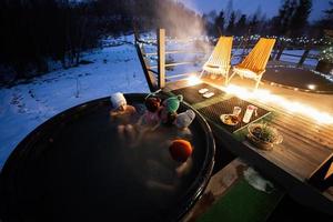 famiglia godendo bagnarsi nel di legno barile caldo vasca nel il terrazza di il villetta. scandinavo vasca da bagno con un' camino per bruciare legna e calore acqua. foto