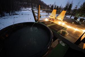 di legno barile caldo vasca nel il terrazza di il Villetta a inverno notte. scandinavo vasca da bagno con un' camino per bruciare legna e calore acqua. foto