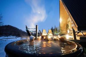 famiglia godendo bagnarsi nel di legno barile caldo vasca nel il terrazza di il villetta. scandinavo vasca da bagno con un' camino per bruciare legna e calore acqua. foto