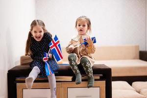 Due sorelle siamo seduta su un' divano a casa con islandese bandiere su mani. Islanda bambini ragazze con bandiera . foto