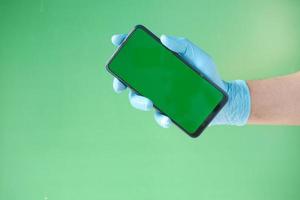 mano in guanti di lattice tenendo smart phone su sfondo verde