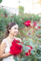 giovane asiatico donna indossare un' bianca vestito pose con un' rosa nel rosa giardino foto