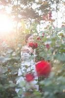 giovane asiatico donna indossare un' bianca vestito pose con un' rosa nel rosa giardino foto