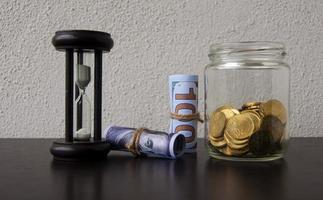 dritto Visualizza di oro monete, banca Appunti e minuti bicchiere con bianca sfondo. concetto foto