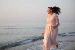 un' bellissimo di mezza età donna nel un' vestito corre lungo il spiaggia. foto
