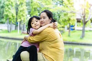 carino giovane figlia con sua madre abbracciare nel amore giocando insieme nel un' parco foto