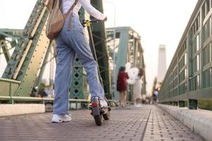 ritratto di giovane bellissimo donna con un elettrico scooter al di sopra di ponte nel moderno città sfondo foto