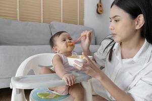 giovane madre porzione bambino mangiare miscela cibo su bambino sedia foto