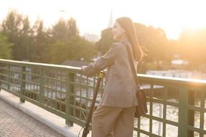 ritratto di giovane attività commerciale donna con un elettrico scooter per opera al di sopra di ponte nel moderno città sfondo foto