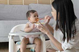 giovane madre porzione bambino mangiare miscela cibo su bambino sedia foto