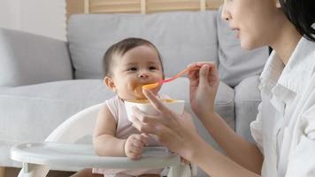 giovane madre porzione bambino mangiare miscela cibo su bambino sedia foto