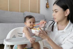 giovane madre porzione bambino mangiare miscela cibo su bambino sedia foto