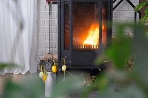 Pasqua arredamento vicino camino stufa con fuoco e legna da ardere. accogliente casa focolare nel interno con in vaso piani, colorato Pasqua uova, Pasqua coniglietto e mazzo. primavera nel un' nazione Casa foto