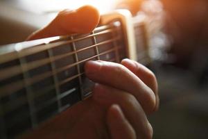 un' dell'uomo mano su il tastiera di un' chitarra corre il suo dita attraverso il stringhe e morsetti il accordi. strumentale musica, chitarra lezione su foglio musica foto