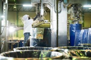 femmina lavoratore nel un' ketchup fabbrica controllato automatico asettico Riempimento macchina Riempimento ketchup in grande tini a un industriale servizio, struttura nel Asia. cibo industria agroindustria. foto