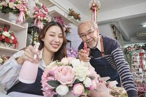 vecchio uomo e giovane bellissimo asiatico femmina fioraio lavoratori acqua spruzzatura un' flora mazzo insieme, contento opera nel un' colorato fiore negozio negozio, fresco fioritura mazzi di fiori decorare, pmi attività commerciale imprenditore. foto