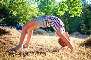 un' poco ragazza fa un' ponte, curvatura sua indietro nel natura. un' flettere foto