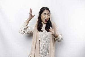 ritratto di spensierato asiatico musulmano donna, avendo divertimento karaoke, cantando nel microfono mentre in piedi al di sopra di bianca sfondo foto