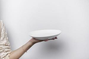 avvicinamento, Tenere un' bianca piatto e cucchiaio, isolato su un' bianca sfondo. foto
