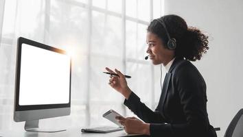 vicino su chiamata centro operatore nel senza fili cuffia parlando con cliente, donna nel cuffie con microfono consulenza cliente su Telefono nel cliente supporto servizio, guardare a computer schermo foto