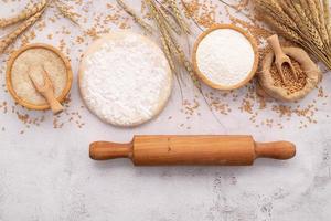 gli ingredienti per l'impasto della pizza fatta in casa con spighe di grano, farina di grano e chicchi di grano allestiti su sfondo bianco di cemento. foto